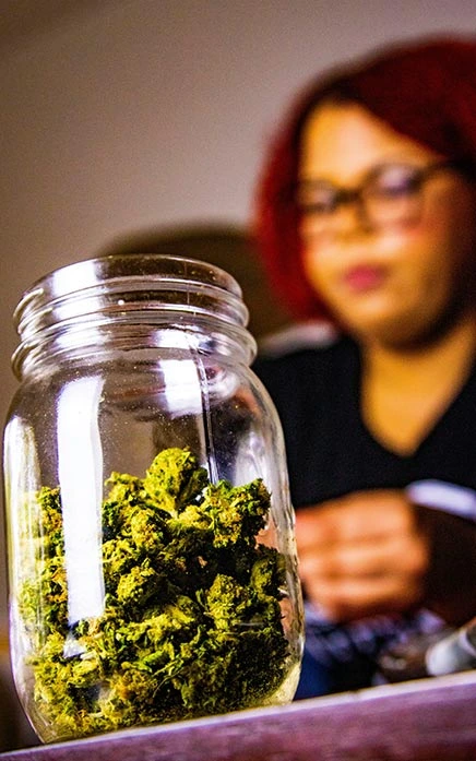 Cannabis flower in a jar, with a lady in the background, out of focus