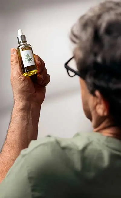 Elderly man in glasses seen from the back, holding a bottle of CBD product in his hand