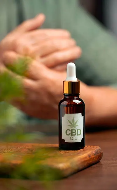 CBD (cannabidiol) oil dropper with hands in the background. For article on cannabinoids in cannabis