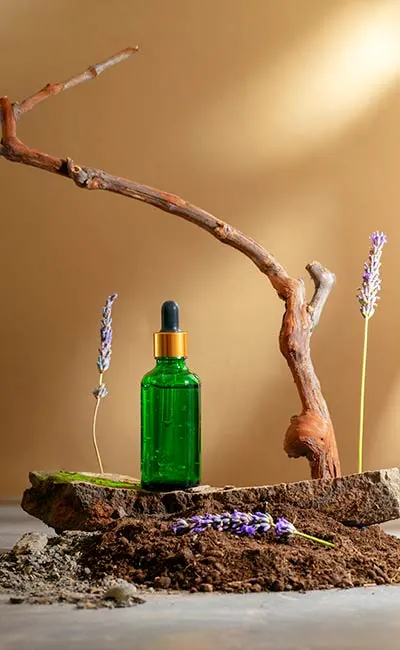 C21+ on Cannabinoids: Cannabis Oil extract in green bottle amid setup of branches and lavender colored plants. Bottle probably has cannabis extract of THC, CBD, or a mix.