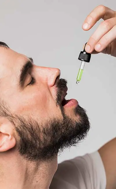 Bearded man using a dropper to consume cannabis