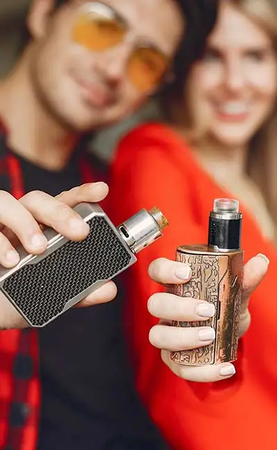 Out of focus couple in background holding cannabis vaping devices